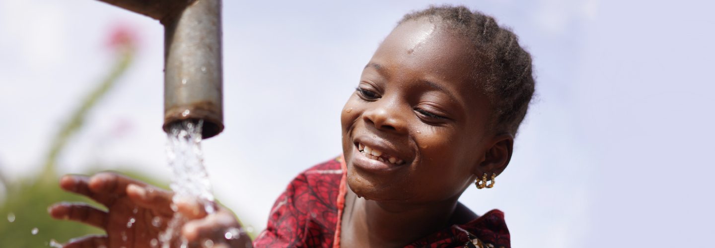 Image of a young girl smiling next to water pump