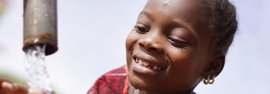 Image of a young girl smiling next to water pump